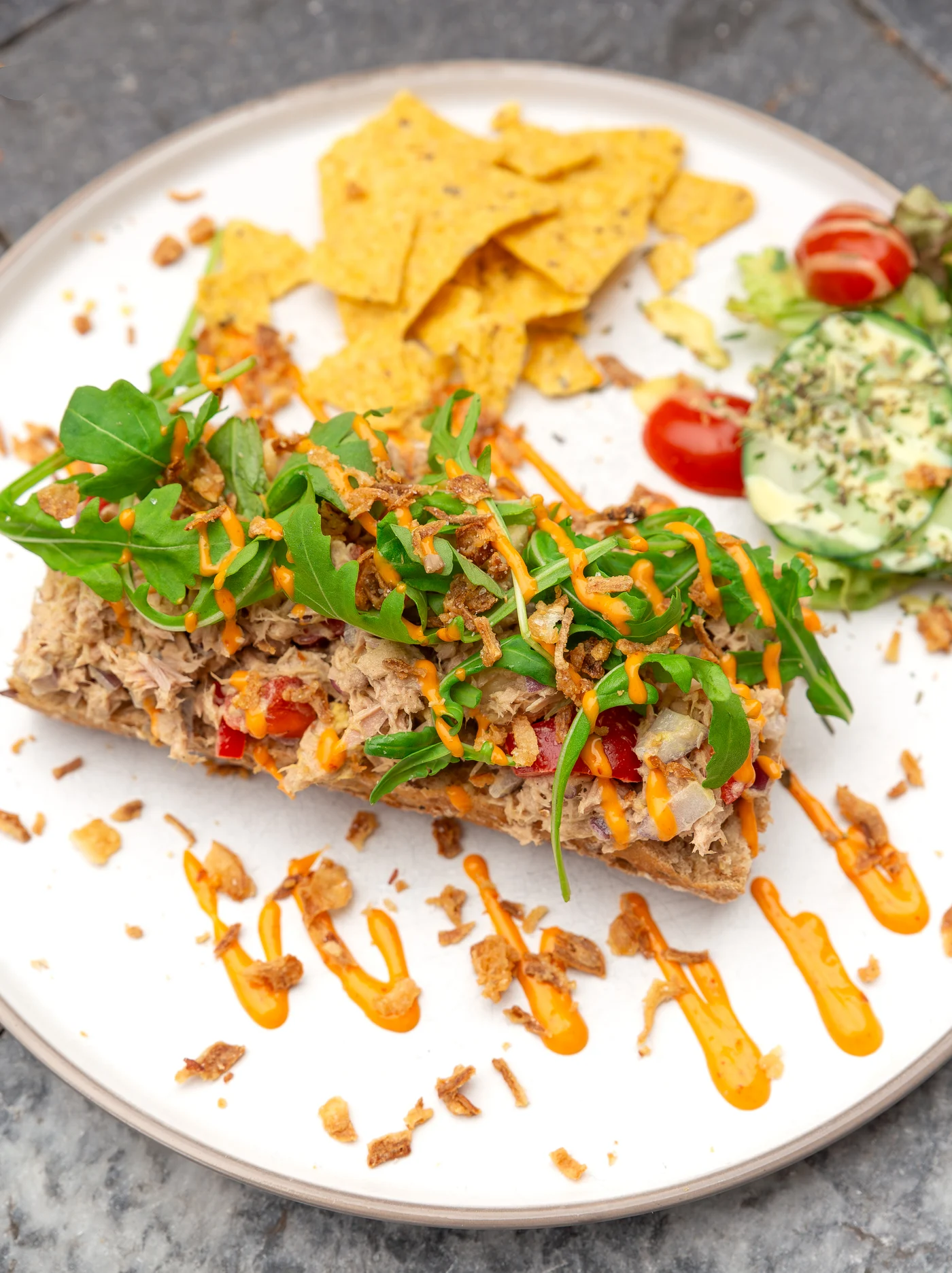 Een broodje tonijn met rucola, geserveerd met chips.
