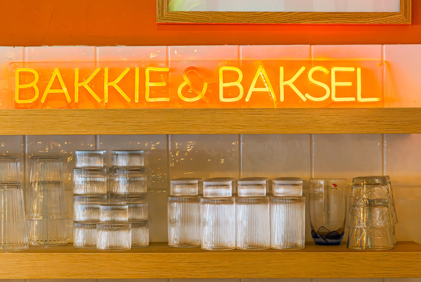 Het verlichte Bakkie & Baksel-logo boven de glazen achter de bar.